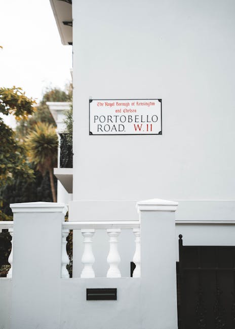 A white residential building with a small front porch featuring a white balustrade composed of turned balusters and square posts. The wall of the building is smooth and painted white, with a black rec